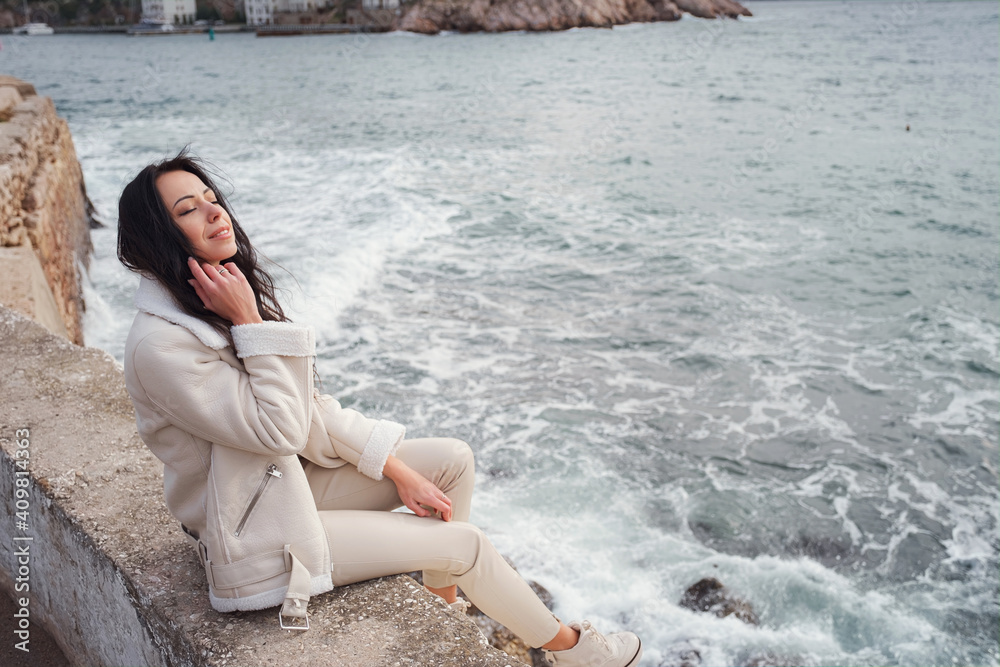 A woman in beige clothing enjoying the view of the sea on a warm, windy day.