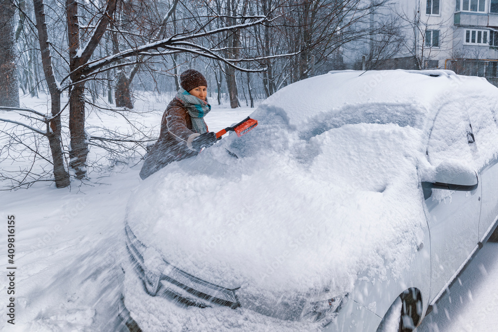 Woman driver cleans windshield of her car from snow.