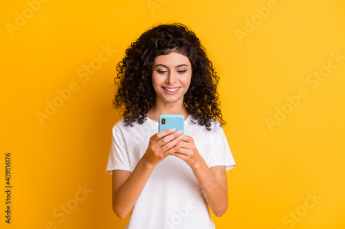 Photo of young happy positive cheerful good mood girl using cellhpone wear white t-shirt isolated on yellow color background