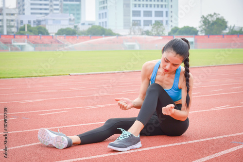Asian female runner sitting on running track suffering from pain at leg after running outdoor.