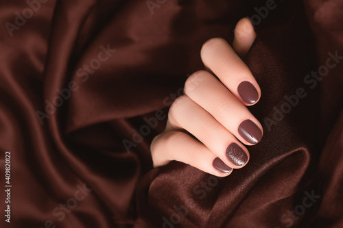 Female hand with brown nail design. Brown nail polish manicure. Woman hand on dark brown fabric background.