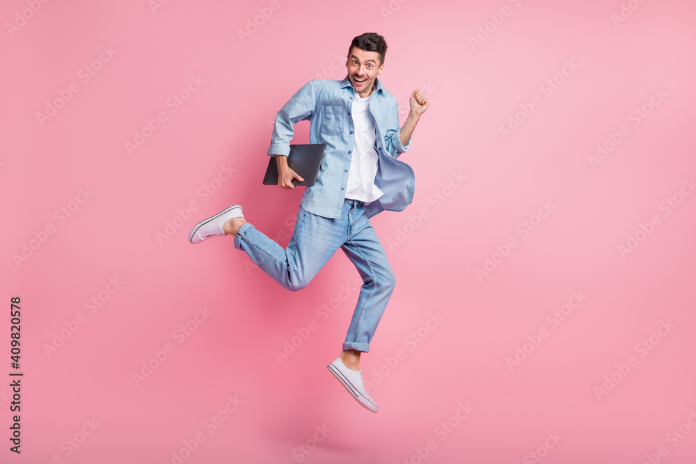 Full size photo of excited happy man hold laptop jump air run sale wear jeans isolated on pink color background
