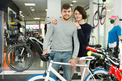.Portrait of smiling guy and girl standing with bicycle in the store