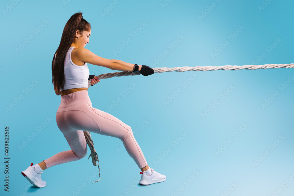 Strong girl athlete pulls the rope on a blue background with empty space.