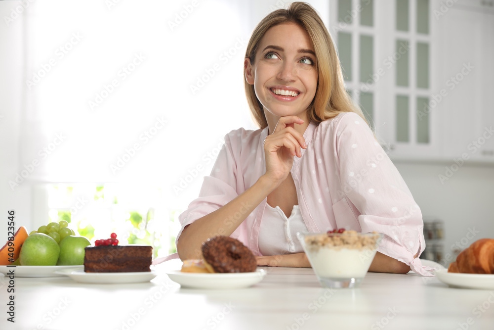 Woman choosing between sweets and healthy food at white table in kitchen Woman choosing between sweets and healthy food at white table in kitchen
