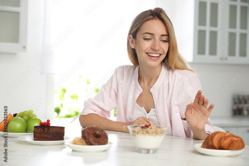 Woman choosing between sweets and healthy food at white table in kitchen Woman choosing between sweets and healthy food at white table in kitchen
