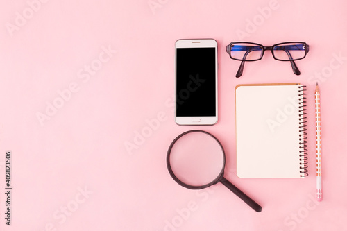 Search or choose a job. Career or freelance concept. Office supplies, notepad and phone and magnifier on a pink pastel background. Copy space, flat lay, top view.