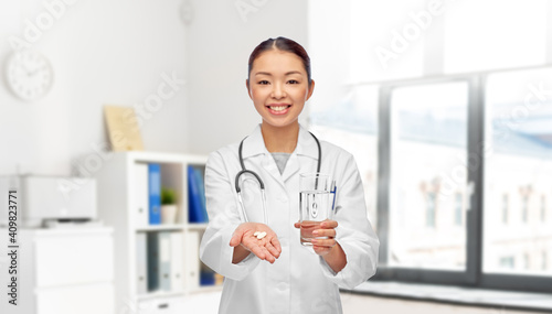 medicine, profession and healthcare concept - happy smiling asian female doctor or nurse pill and glass of water over medical office at hospital on background