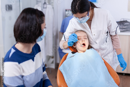 Young stomatolog using curved mirror to check Dentistry specialist during child cavity consultation in stomatology office using modern technology. photo