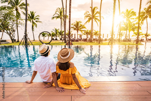 Fotografia Young couple traveler relaxing and enjoying the sunset by a tropical resort pool