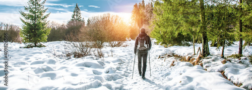 Popular winter outdoor activities. Male hiker hiking with backpack and Nordic walking poles in the snow.