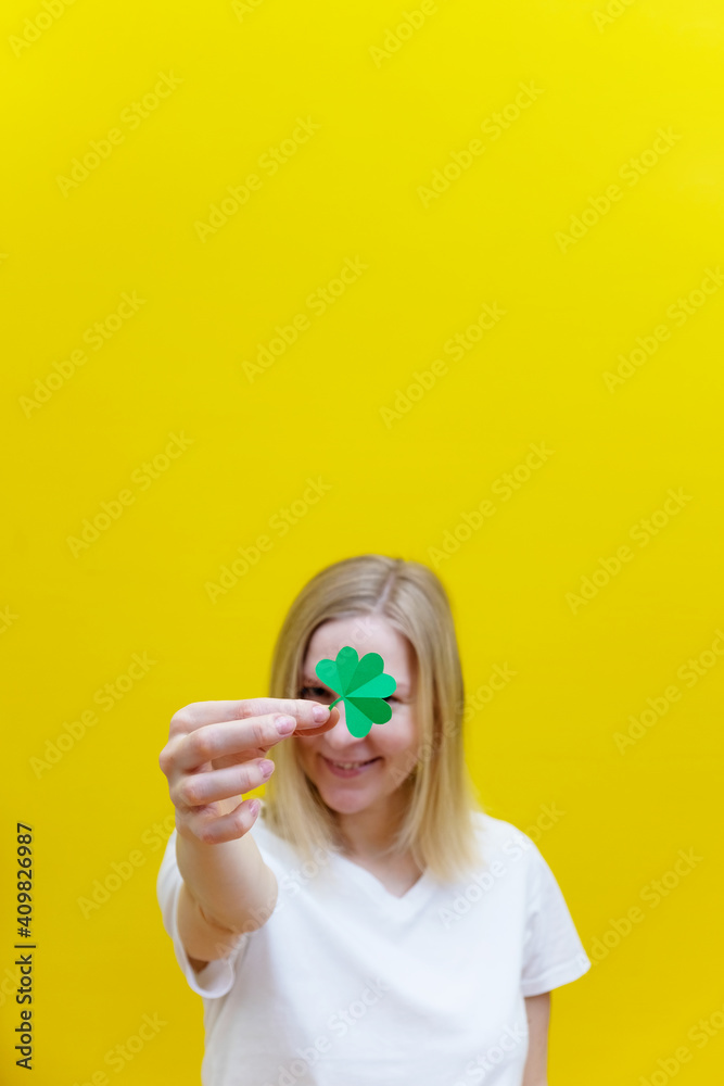 Shamrock in hand of young women in front of her face. Girl's face on yellow background. Selective focus. Shamrock in hand of young women in front of her face. Girl's face on yellow background. Selective focus.