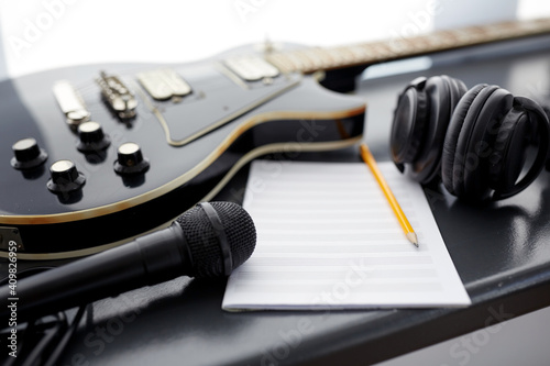 composing and music writing concept - close up of bass guitar with music book, microphone and headphones on black table