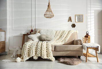 Cozy living room interior with beige sofa, knitted blanket and cushions