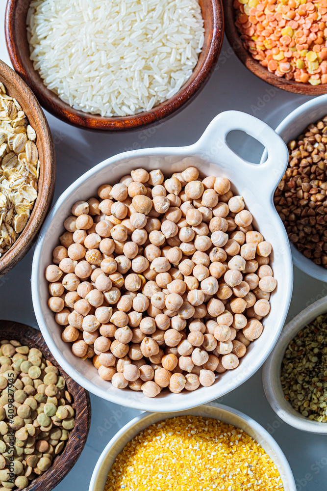 Raw chickpeas in white bowl. Various dry cereals and legumes in white and wooden bowls, white background. Vegan protein concept. Raw chickpeas in white bowl. Various dry cereals and legumes in white and wooden bowls, white background. Vegan protein concept.