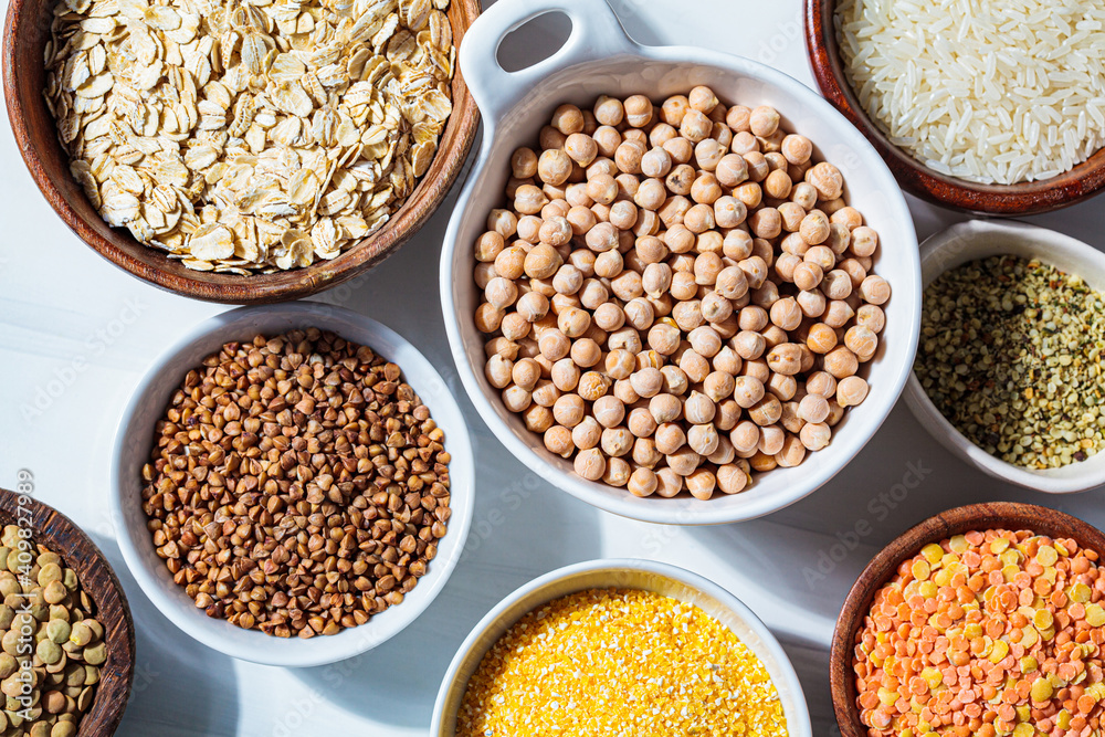 Raw chickpeas in a white bowl. Various dry cereals and legumes in white and wooden bowls, white marble background. Vegan protein concept. Raw chickpeas in a white bowl. Various dry cereals and legumes in white and wooden bowls, white marble background. Vegan protein concept.
