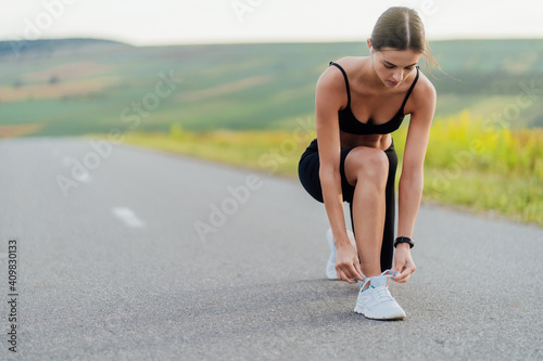 Sports concept. Athletic girl on the road during the run stopped to tie shoelaces to sneakers