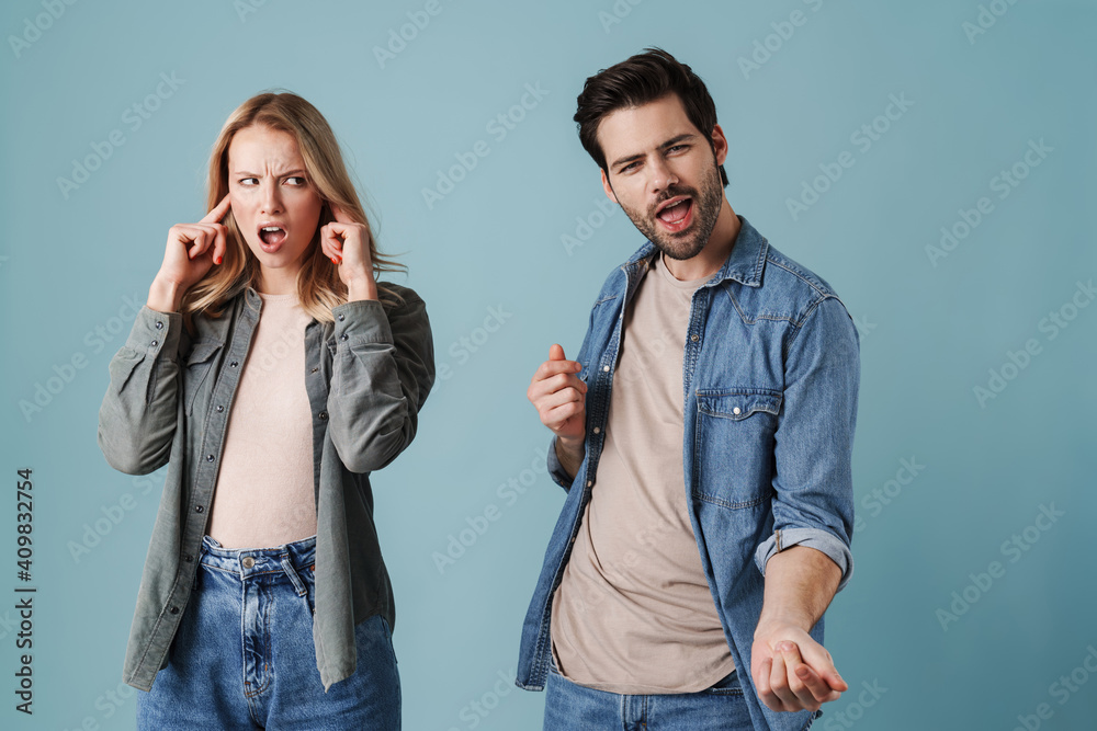 Excited man singing and dancing while his girlfriend plugging her ears Excited man singing and dancing while his girlfriend plugging her ears