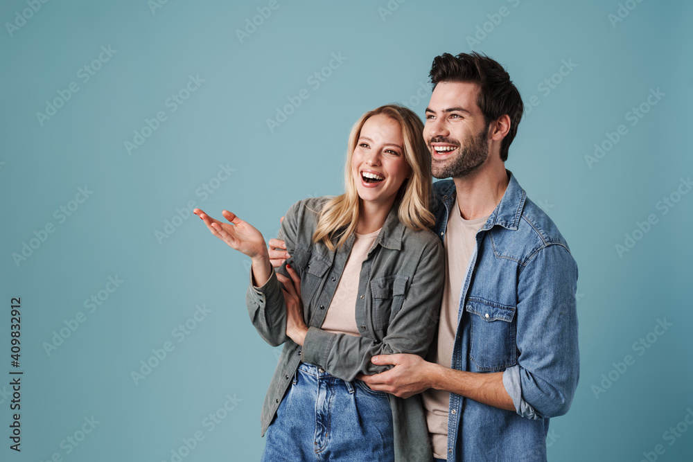 Young beautiful excited man and woman hugging and pointing finger - obrazy, fototapety, plakaty 