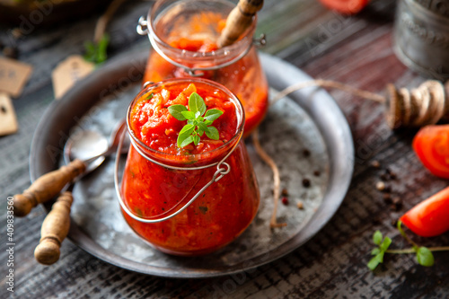 homemade red tomato sauce in glass jar on metal plate on wooden table with basil leaves