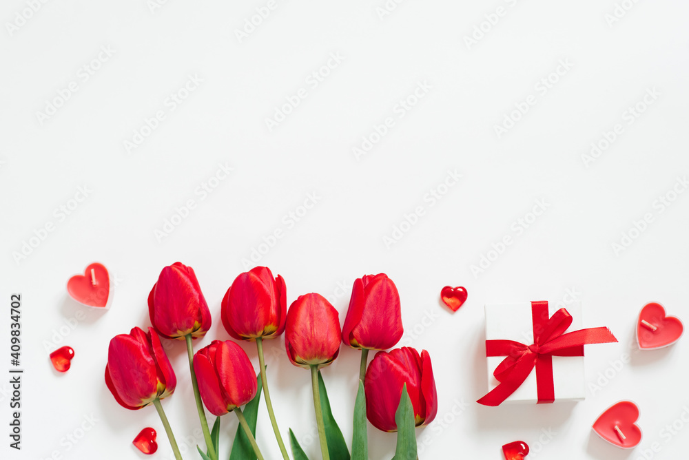 Valentine Day Romantic Background. Red tulips, a gift with a bow, and candle hearts on a white background with copying space. Flat lay Valentine Day Romantic Background. Red tulips, a gift with a bow, and candle hearts on a white background with copying space. Flat lay