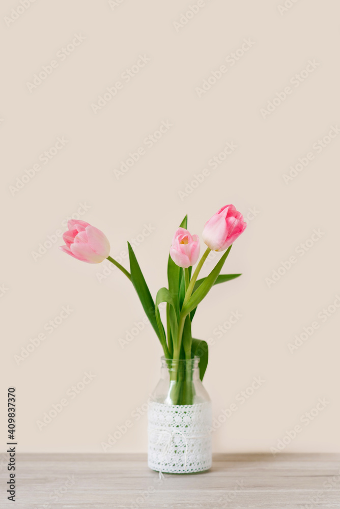 A bouquet of three pink tulips stands in a glass vase with lace. The concept of the spring festival