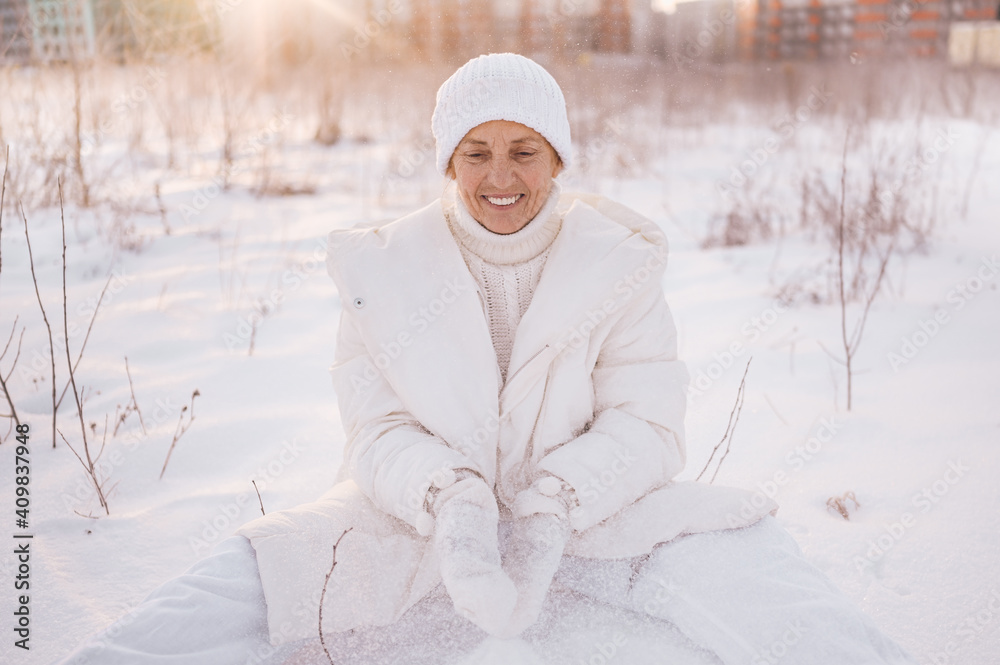 Obraz premium Happy elderly senior mature woman in white warm outwear playing with snow in sunny winter outdoors. Retired healthy people holiday vacation winter activities, active lifestyle concept.