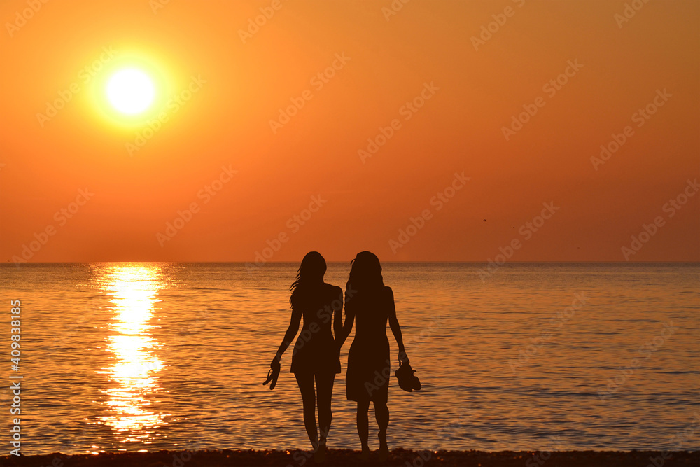 Two  young women holding hands walking barefoot with slippers in his hand on the beach