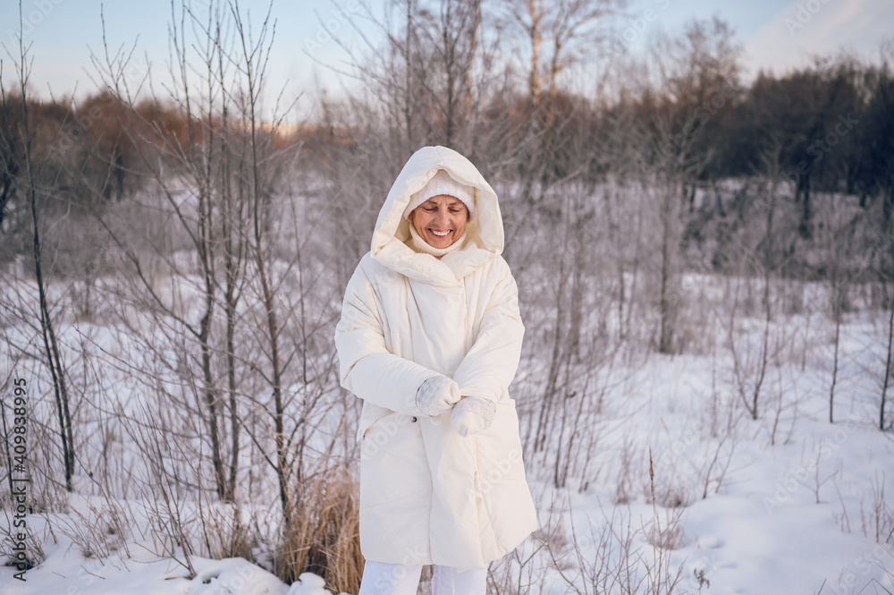 Obraz premium Happy elderly senior mature woman in white warm outwear playing with snow in sunny winter outdoors. Retired healthy people holiday vacation winter activities, active lifestyle concept.