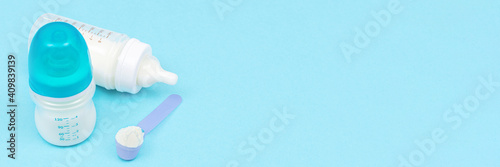 Banner with milk powder for baby in measuring spoon near baby bottles on blue background