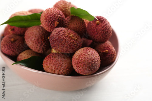 Fresh ripe lychees in bowl on white wooden table, closeup