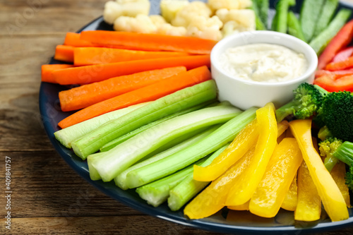 Plate with celery sticks, other vegetables and dip sauce on wooden table, closeup
