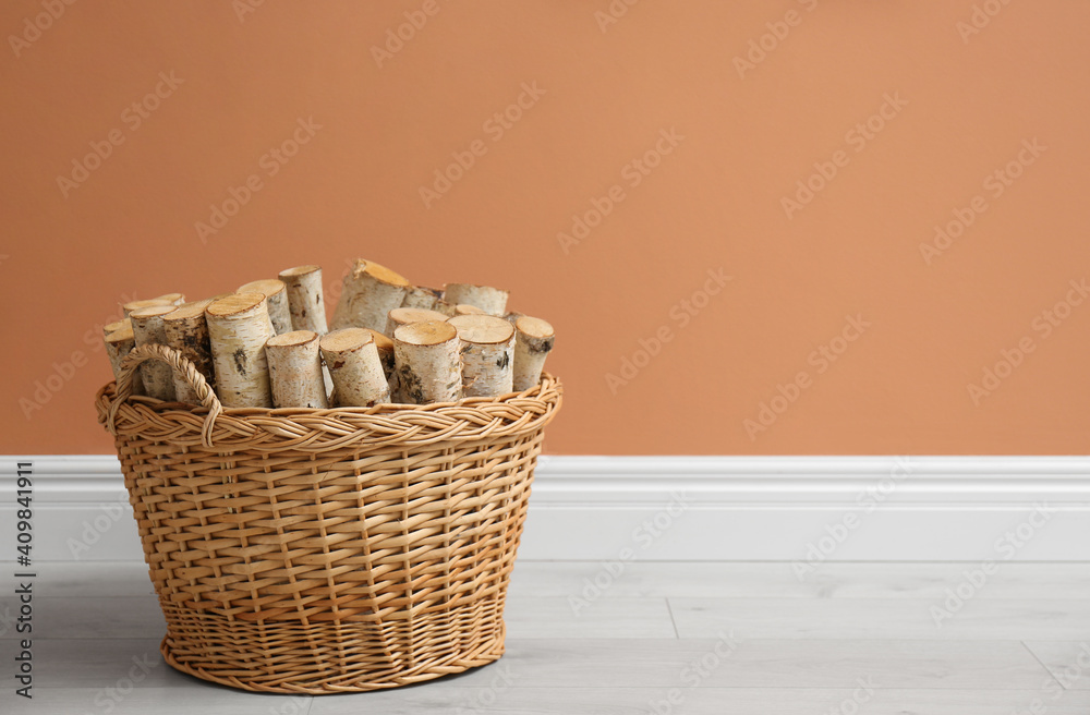 Wicker basket with firewood near brown wall indoors, space for text Wicker basket with firewood near brown wall indoors, space for text
