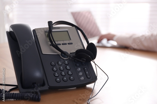 Desktop telephone with headset on wooden table in office. Hotline service