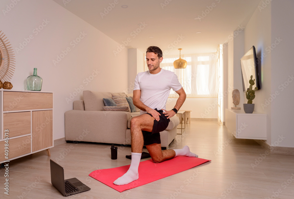 Young man stretching psoas at home in front of a laptop..Online workout..Home training concept. Young man stretching psoas at home in front of a laptop..Online workout..Home training concept.