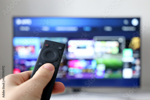 Male hand with remote controller on smart TV screen background. Person choosing streaming services, watching movies