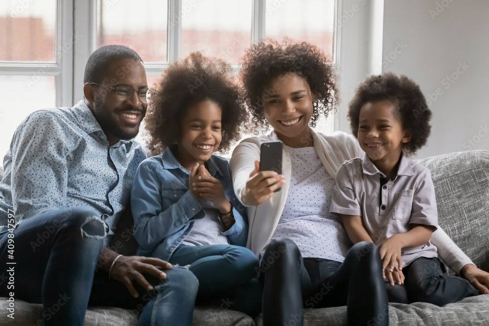 Close up happy African American family taking selfie on phone or making video call together, smiling mother holding smartphone, photographing with husband and kids, sitting on cozy couch at home Close up happy African American family taking selfie on phone or making video call together, smiling mother holding smartphone, photographing with husband and kids, sitting on cozy couch at home