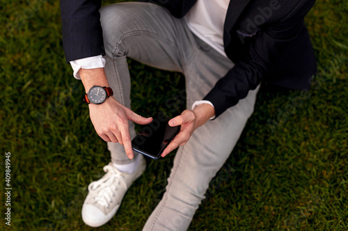 Stylish man sitting on grass and using smartphone