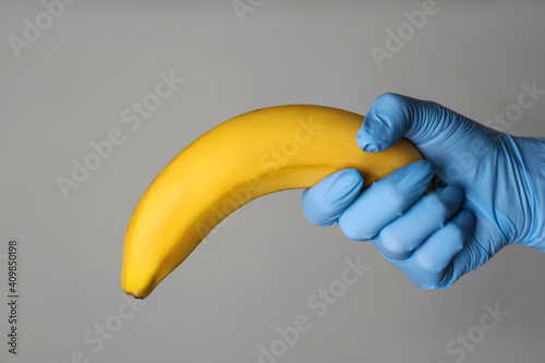 Foto Doctor holding banana symbolizing male sexual organ on grey background, closeup