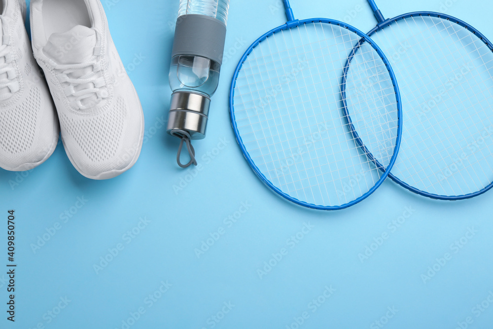 Fototapeta premium Badminton rackets, bottle and shoes on light blue background, flat lay. Space for text