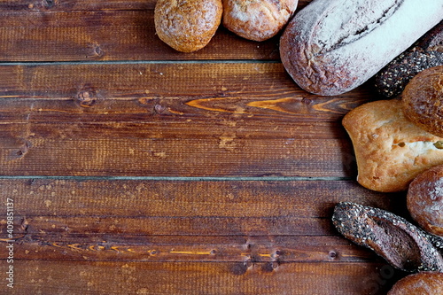 Freshly baked bread of various shapes lies on a brown wooden surface.Copy space. Top view.