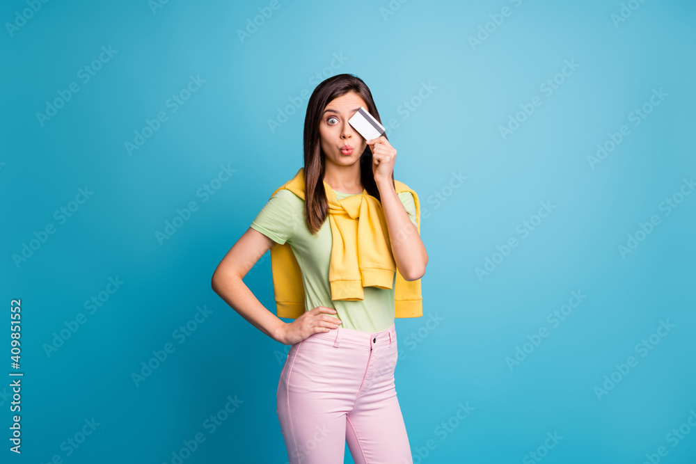 Portrait of pretty lady put hand on waist lips wow hold debit card covering eye isolated on blue color background Portrait of pretty lady put hand on waist lips wow hold debit card covering eye isolated on blue color background