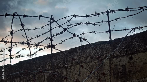 Floating dramatic clouds behind a concrete wall with barbed wire,  timelapse concept. photo