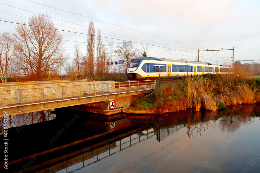 SLT local commuter train during sunset at track in Zevenhuizen crossing river Rotte SLT local commuter train during sunset at track in Zevenhuizen crossing river Rotte
