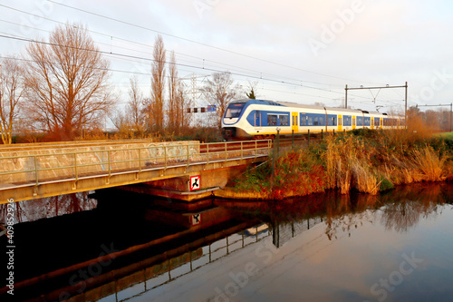 SLT local commuter train during sunset at track in Zevenhuizen crossing river Rotte