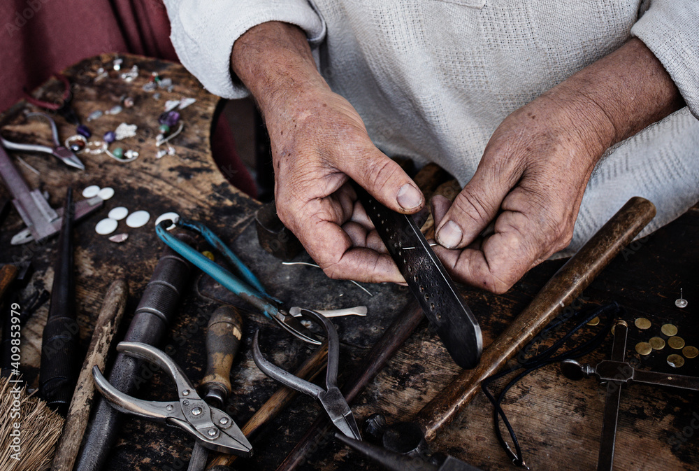 Closeup of an old caucasian man handcrafting a ring with its tools.