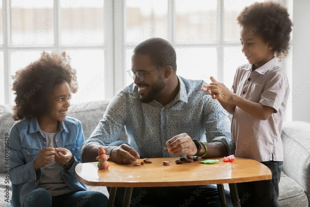 Happy African American father and kids playing with colorful plasticine ...