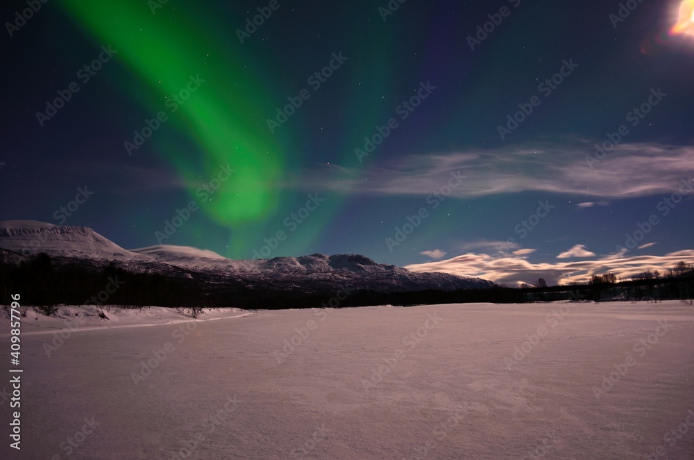 strong aurora borealis, northern light, over snowy mountain and moon lit landscape in the arctic circle night
