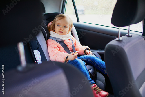 Adorable toddler girl in modern car seat eating cookie