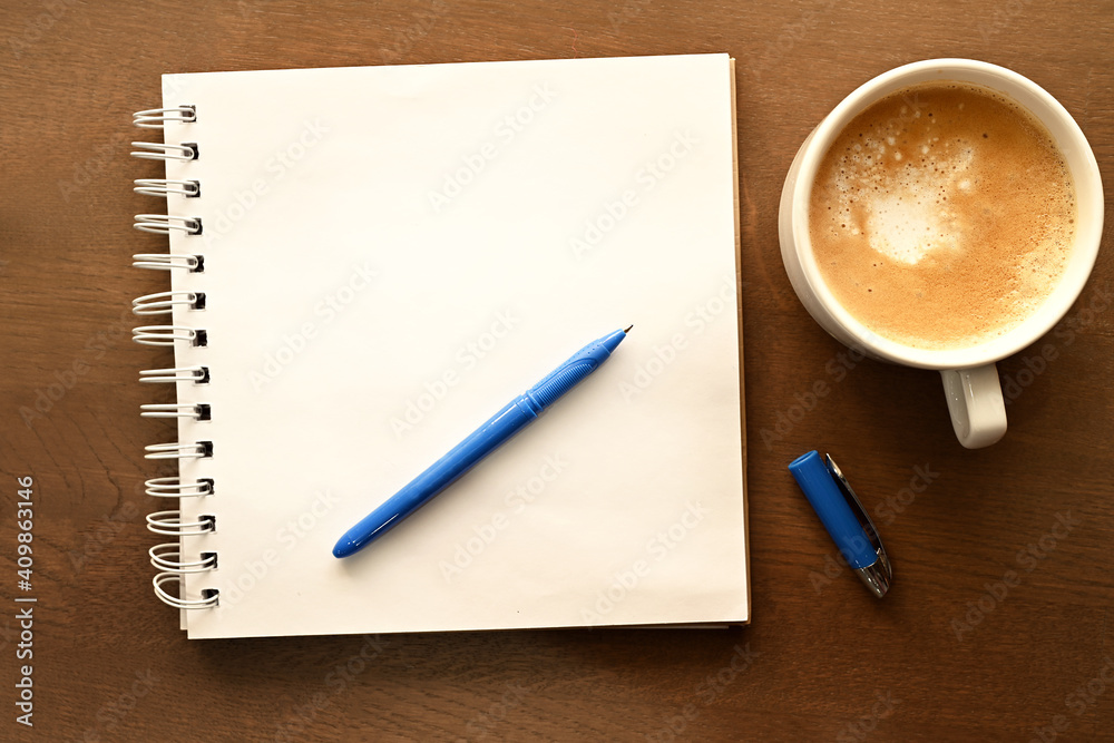 Desktop. Notepad, blue pen and a cup of coffee stand on a wooden table. Desktop. Notepad, blue pen and a cup of coffee stand on a wooden table.